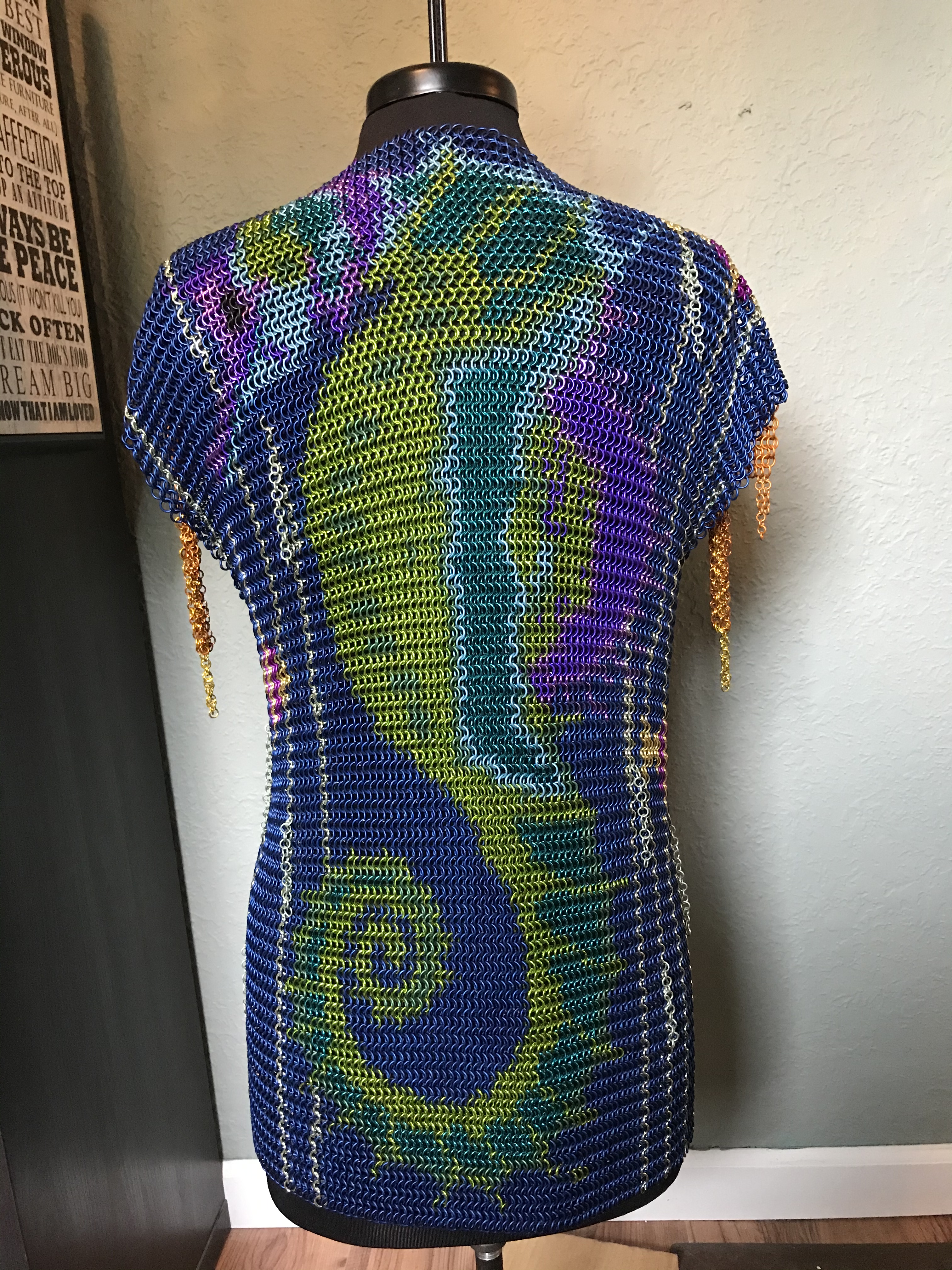 a chainmaille shirt with two colorful seahorses facing each other in pink, purple, blue, green, and yellow rings on a deep blue background, with bronze chain fringe sleeves.
