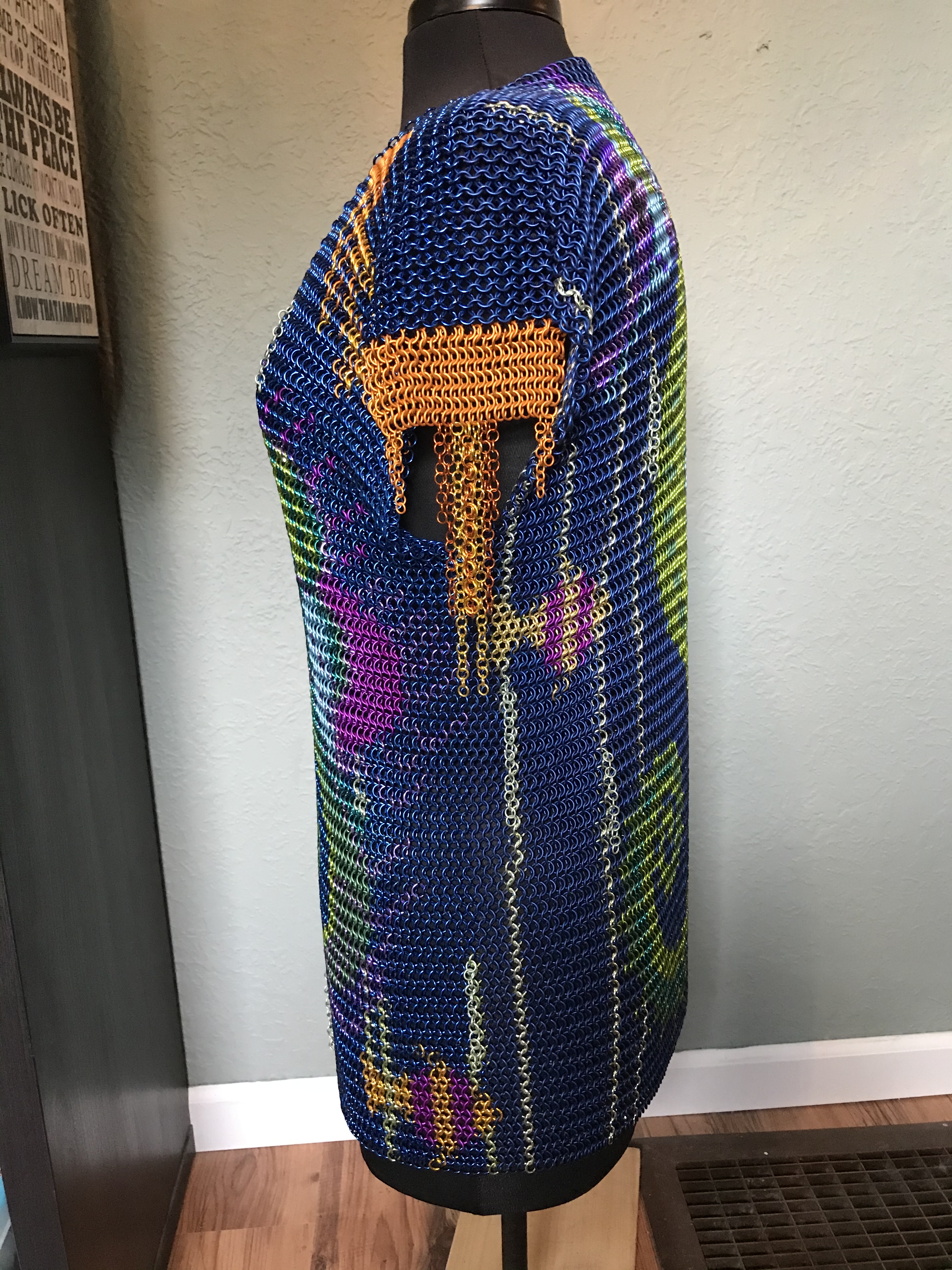 a chainmaille shirt with two colorful seahorses facing each other in pink, purple, blue, green, and yellow rings on a deep blue background, with bronze chain fringe sleeves.
